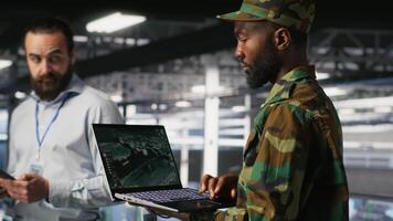 Drone operators in military data center supervising autonomous flight systems through laptop interface. Teamworking army IT experts doing live drone tracking using notebook, camera B video