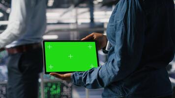 Server hub engineers finetuning configurations using chroma key device. Close up of technicians on data center industrial platform analyzing performance outputs on isolated screen tablet, camera B video
