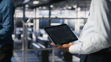 Close up of data center admin using tablet to reviewing machine learning code dashboards. Server farm IT expert using device to monitor AI infrastructure performance, camera B video