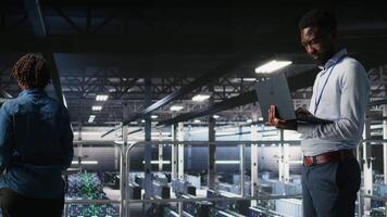 Engineers in data center using laptop to monitor neural network LLM visualization. Coworkers on server hub industrial platform overseeing server clusters powering machine learning processes, camera A video