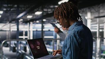 Technician in data center stressed by critical error popup on laptop during diagnostics session. Anxious IT specialist troubleshooting system fault affecting infrastructure performance, camera B video