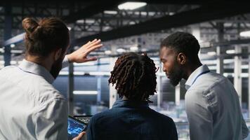 Data center manager talking with workers performing maintenance on supercomputers used for AI. Server hub team leader and staff members upgrading rigs used for deep learning training, camera B video