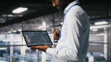 Close up of programmer swiping on tablet display in data center, doing maintenance tasks, ensuring optimal performance. IT expert checks code on device, applying patches to improve stability, camera B video
