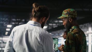 Military technician reviewing tactical dashboard on laptop screen inside secure server hub. Army expert using strategic communications and infrastructure oversight software on notebook, camera B video