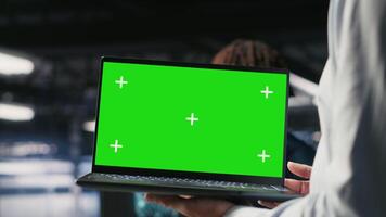 Close up of data center employee doing maintenance tasks on green screen laptop, ensuring optimal performance. Worker using mockup notebook to review diagnostics and apply patches, camera B video