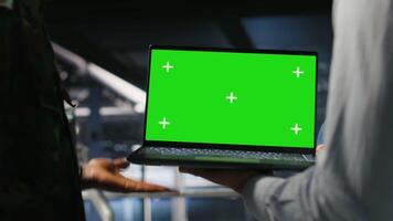Army engineering team in command center server hub using mockup laptop to install and maintain IT systems. Military data center admins overseeing information systems with chroma key notebook, camera B video