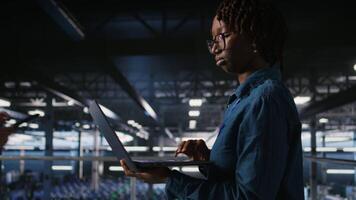 Data center computer scientist doing maintenance tasks on laptop, ensuring optimal performance. African american technician reviewing diagnostics and applying patches to server hub gear, camera A video