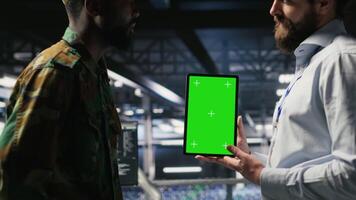 Military personnel overseeing AI computing operations on isolated screen tablet in high tech server facility. Army tech experts using chroma key device to oversee communication systems, camera B video