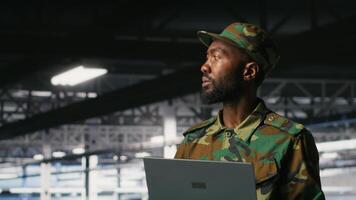Army information technology specialist in data center troubleshooting military computer systems and networks using laptop. Soldier in command center server room using notebook, camera B video