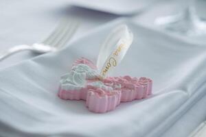 Decorative cross shaped ornament with floral details and angel motif on a folded napkin, with a fork and glass in a refined dining setting. photo