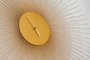 A modern wall clock with a golden circular face, minimalist hands, and radiating metal rods, mounted on a plain white background. photo