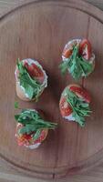 Fresh bruschetta with tomatoes and arugula on a wooden plate, A hand arranging bruschetta topped with tomatoes and arugula. video
