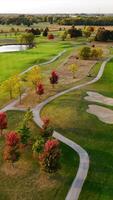 Aerial View of Scenic Golf Course in Autumn. Expansive golf course with lush green fairways, sand bunkers, winding paths, and colorful autumn trees under a video