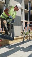 Construction Worker Drilling on Building Site. A construction worker is seen drilling into a concrete slab on a building site, wearing a high-visibility vest video