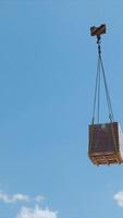 Crane lifting pallet of bricks at construction site, A crane lifting a pallet of bricks high into the air at a construction site, set against a clear blue sky video