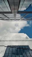 Upward view of modern skyscrapers against a cloudy sky Time lapse, A striking upward perspective of modern glass skyscrapers reaching into a partly cloudy sky, video