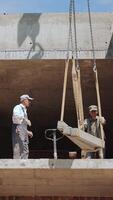 Construction Workers Managing Concrete Slab Placement. Two construction workers are overseeing the placement of a concrete slab on an upper level of a building video