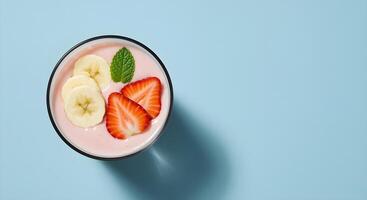 A refreshing smoothie bowl with vibrant strawberries, banana slices, and mint against a blue backdrop. photo