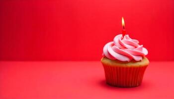 A single cupcake with pink frosting and a lit candle is set against a solid red background. photo