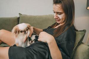 woman in black silk robe grooming fluffy dog on sofa, relaxed morning routine, concept of pet care and leisure time photo