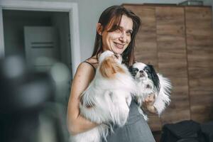 woman tenderly holding two japanese chin dogs, showcase affection and pet care at home photo