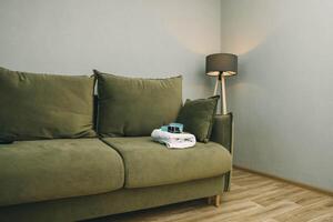 spa skincare products on folded white towel resting on green sofa with large cushions, cozy living room interior with modern tripod floor lamp and grey walls, wellness, home comfort photo