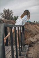 unrecognizable woman in white shirt standing barefoot on wooden platform with one foot raised, natural cliff landscape, back view, solitude, personal reflection, nature retreat photo