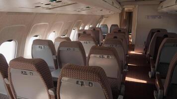 A spacious airplane cabin with empty rows of seats is illuminated by afternoon sunlight, highlighting the calm atmosphere inside the aircraft. video
