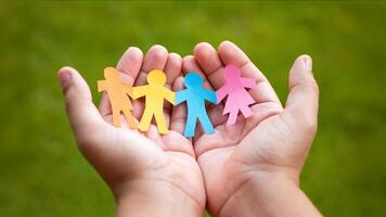 Open hands holding a chain of colorful paper people cutouts symbolizing diversity, inclusion, and teamwork, against a blurred green background photo