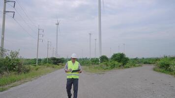 Wide engle and following camera shot. Engineer working with laptop at wind turbine field generating electricity for renewable clean energy video