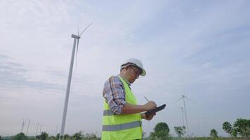 Lower angle shot of engineer is checking and working with tablet at wind turbine field that generating electricity. video