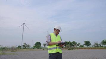 Wide engle camera shot. Engineer working with laptop at wind turbine field generating electricity for renewable clean energy video