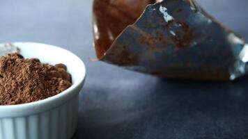 Cocoa powder in white bowl on dark surface with spilled pack video
