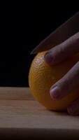 Man's hand skillfully cutting a fresh orange in a dimly lit kitchen setting during early evening video