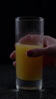 Woman's hand reaching for a cold glass of freshly squeezed orange juice in a dimly lit setting video