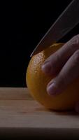 Man cuts fresh orange on wooden cutting board with a sharp knife in a cozy kitchen setting during the afternoon video