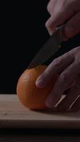Slicing a fresh orange on a wooden cutting board with careful hands and a knife in a dimly lit kitchen setting video