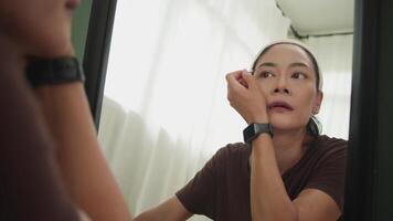 Front view of a woman carefully shaping her eyebrows while looking into a mirror during her makeup routine video