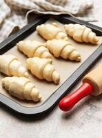 Raw croissants baking on tray with rolling pin and a towel photo