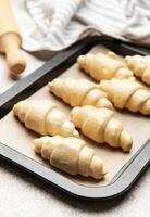 Raw croissants baking on tray with rolling pin and towel photo