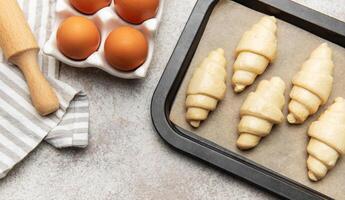 Freshly made croissants resting on baking sheet await oven's warm embrace photo