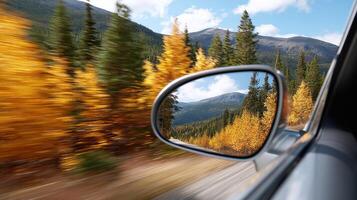 Autumn forest landscape with colorful trees and mountains reflected in car side mirror on sunny day photo