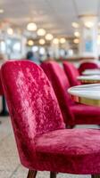 A close-up of a plush, pink velvet chair in a dining setting, featuring a round table with a gold trim. Soft lighting illuminates the background, enhancing the cozy ambiance. photo