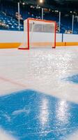 A close-up view of an ice rink, showcasing a bright, polished surface with reflections. The orange goalpost stands prominently against blue markings and empty seats. photo