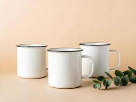 Three white enamel mugs with black rims, arranged on a beige surface with a small branch of green leaves nearb - Rustic Beverage Concept photo