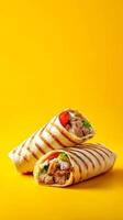 Two wraps with grilled stripes filled with meat and vegetables sit against a bright yellow background photo