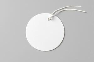 A blank, round, white tag with a string hanging against a gray background, emphasizing its simplicity and space for customization. photo
