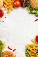 Top-down shot featuring burgers, fries, sauces, greens, and a tomato surrounding empty space photo