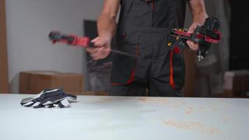 Carpenter lays out drill, clamps and gloves on table with sawdust. Close up of man preparing tools for woodwork on workbench in workshop. Worker preparing for carpentry work video