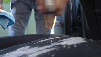 Close up of person is spraying cleaning foam on car seat and wiping it with microfiber cloth. during interior cleaning. Vehicle upholstery maintenance video